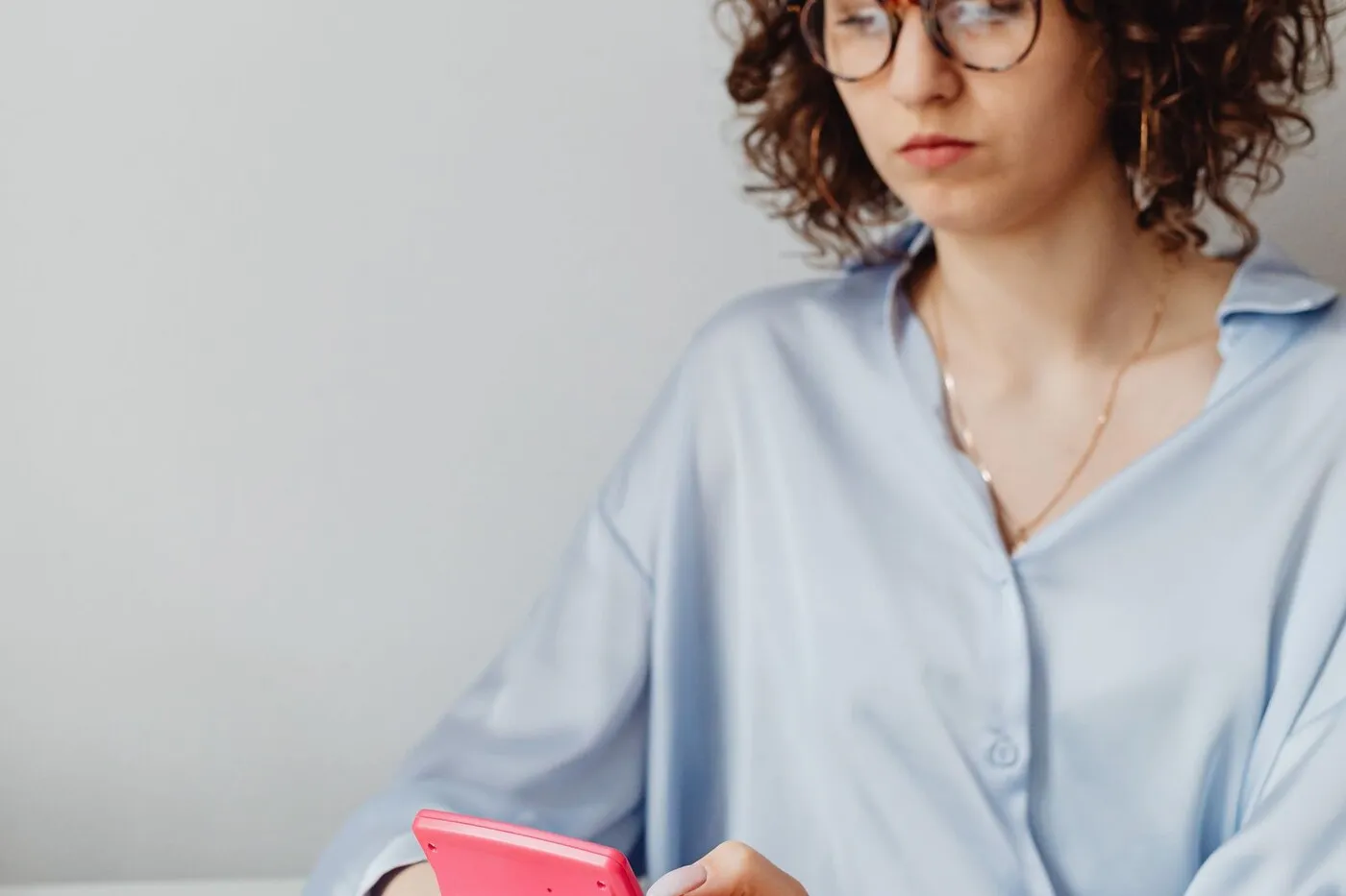 A person in reading glasses going through a stack of printed pages with a calculator at hand.