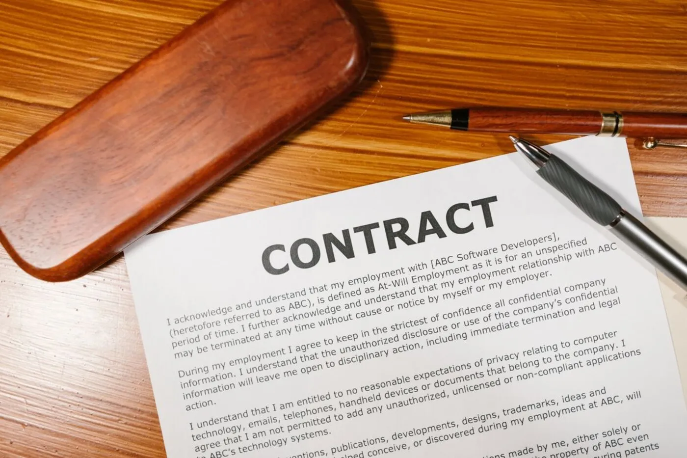 A printed contract document on a wooden desk with two pens resting beside it.