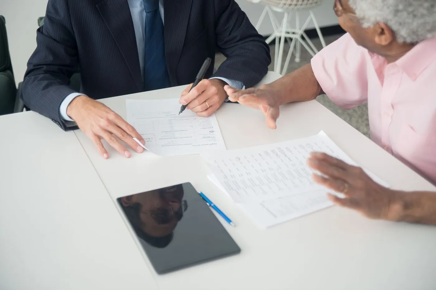 An advisor and an older woman reviewing printed documents together across a white table.