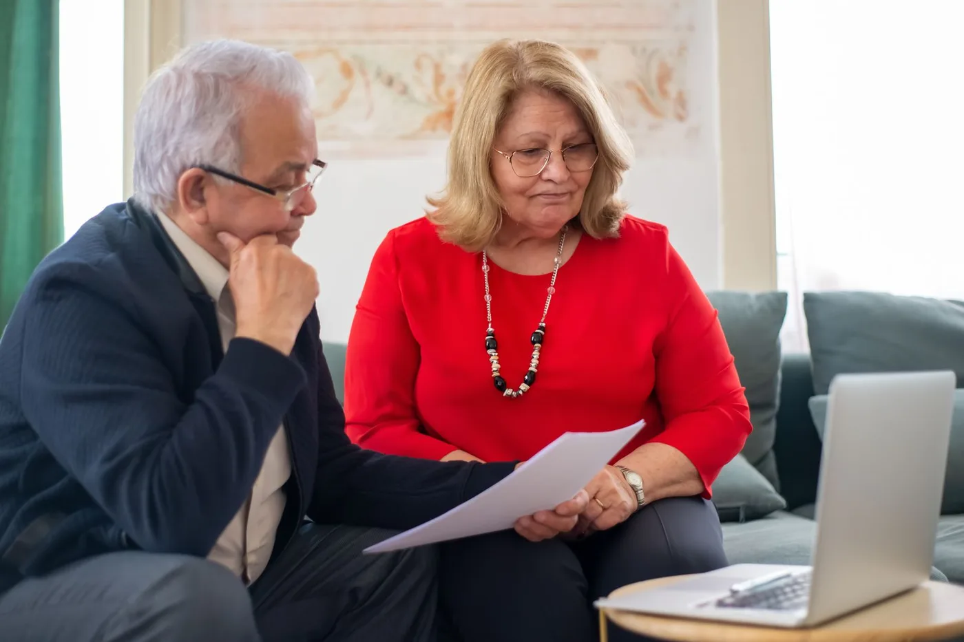 An older couple reviewing financial documents together on a laptop at home.