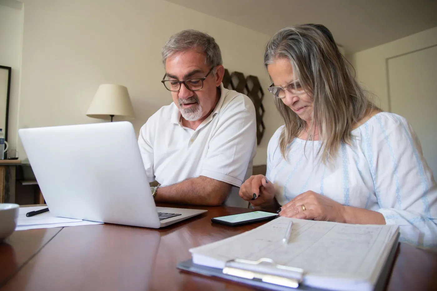 An older adult reviewing paperwork with a laptop open at home.