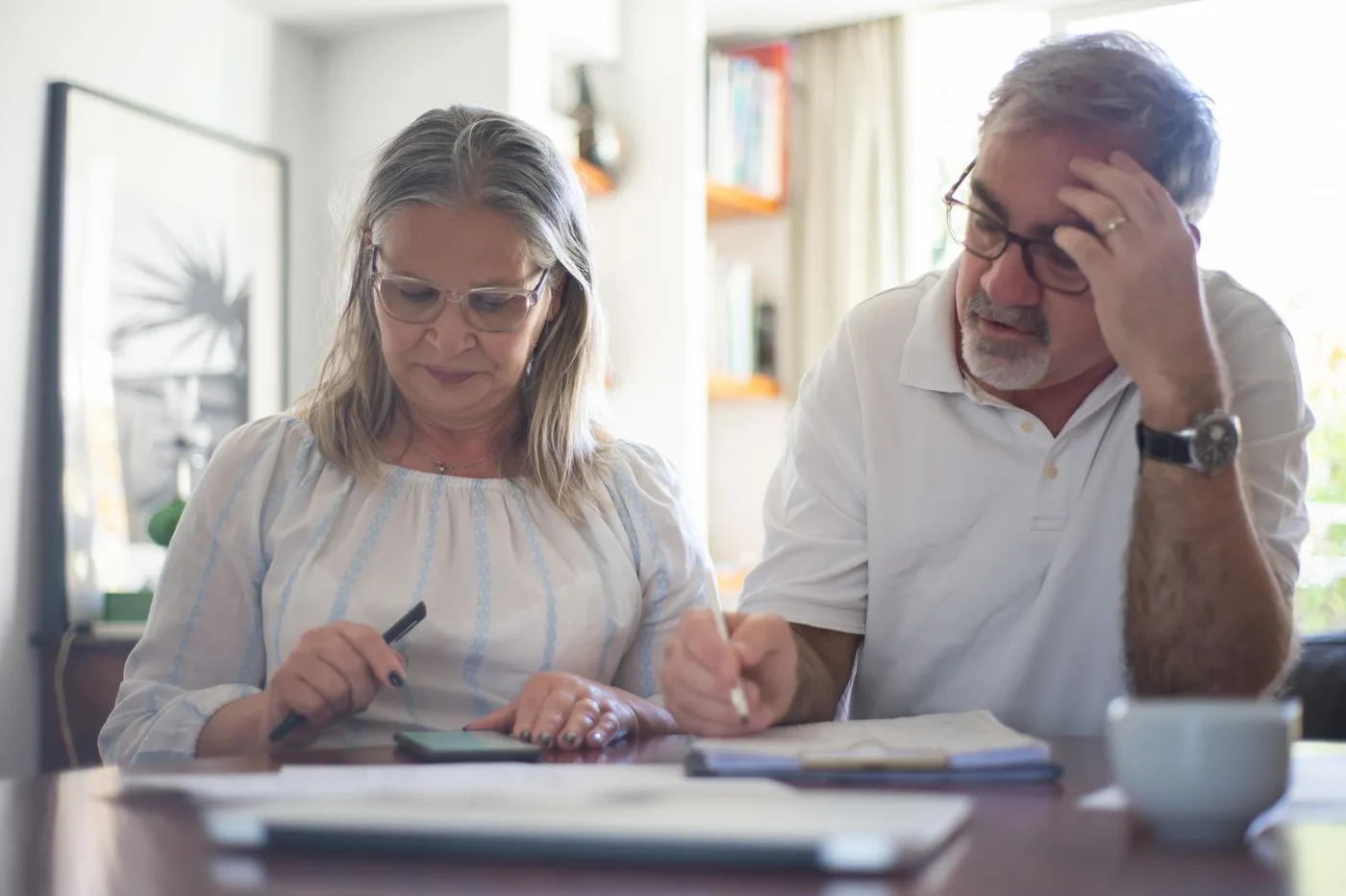 An elderly man reviewing financial paperwork at a home office desk.