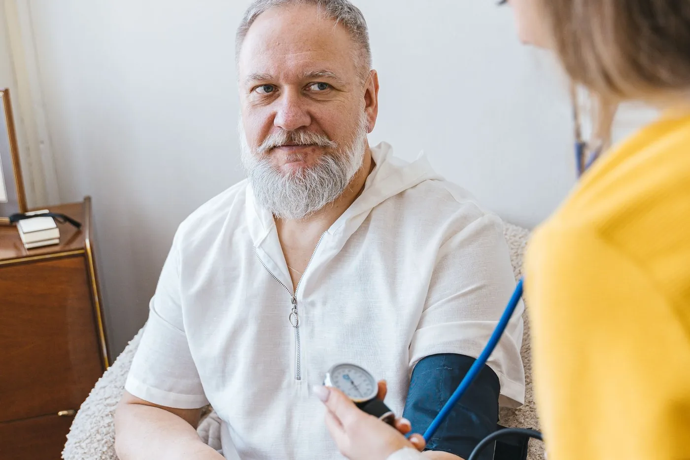 A caregiver checking an elderly man's blood pressure in a home-like setting.