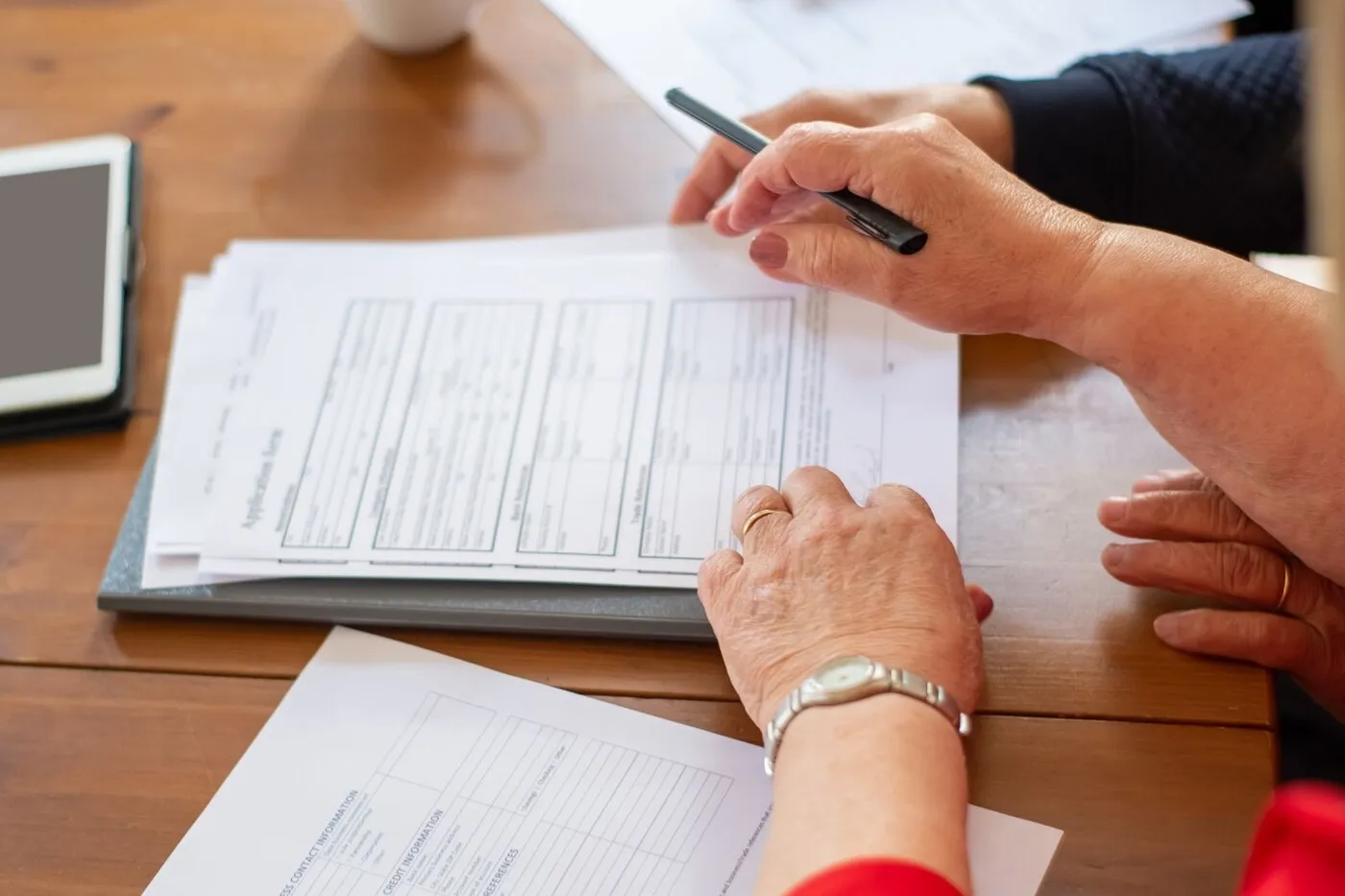 Printed contracts, a tablet, and coffee cups arranged on a meeting table.