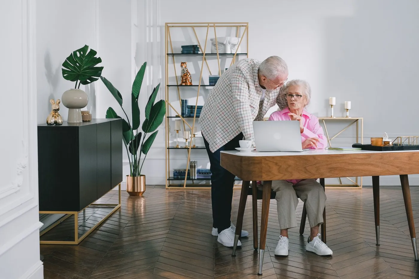 An older couple discussing paperwork together while looking at a laptop at home.