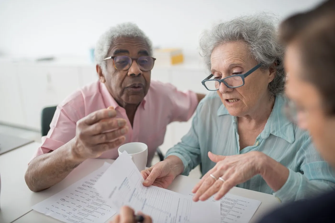 An older adult and a family member talking with a staff member across a table in a bright common room.