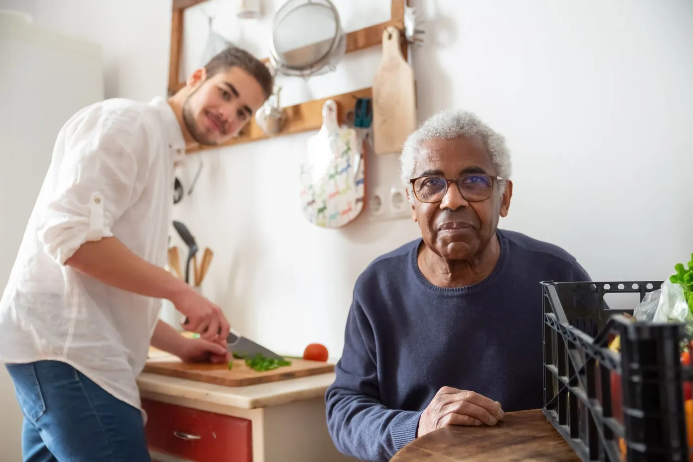 A young caregiver helping a senior man in his own home kitchen.