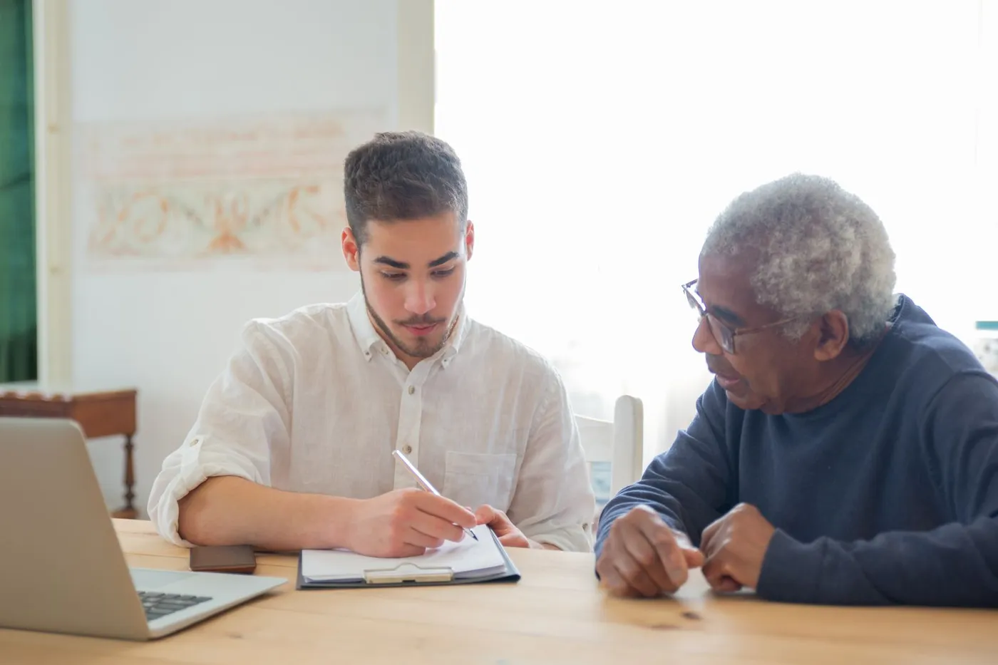 A caseworker helping an elderly man review housing assistance documents at a desk.