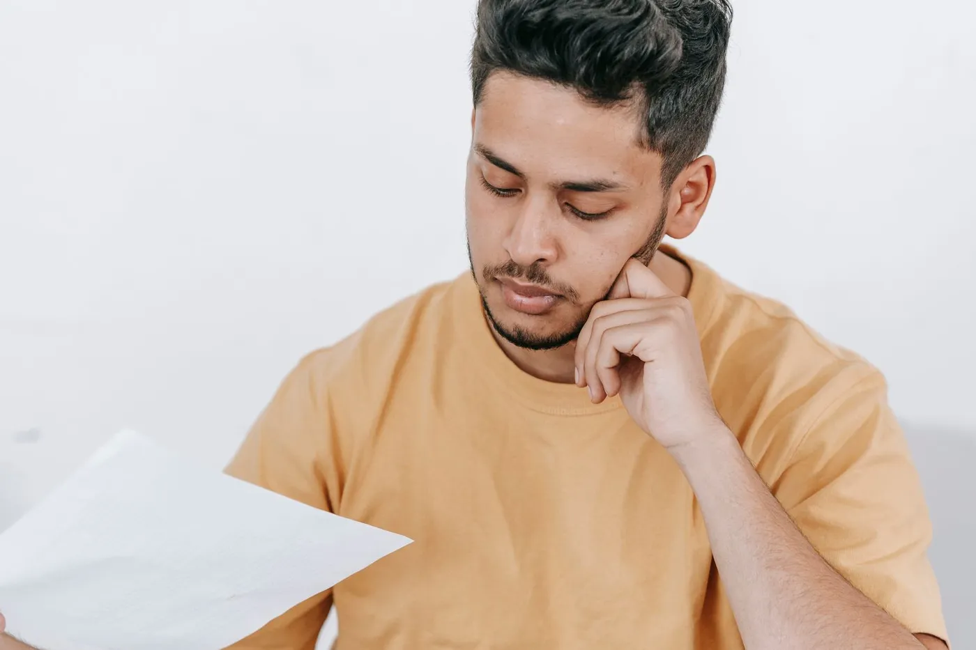 An adult son reviewing financial paperwork at a table with a laptop at home.