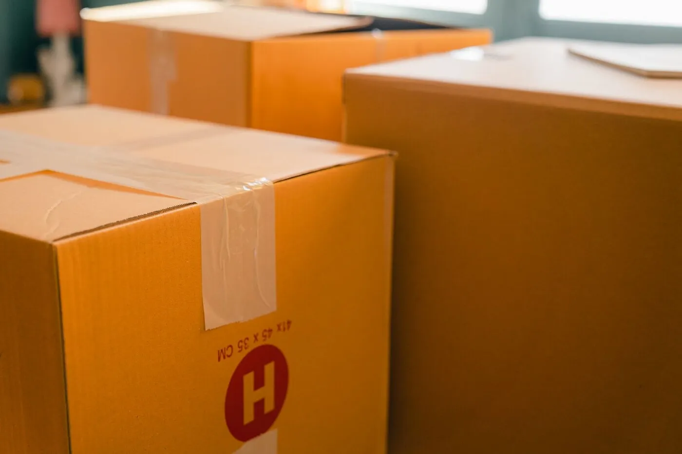 Sealed cardboard moving boxes stacked near a sunlit window in a home.
