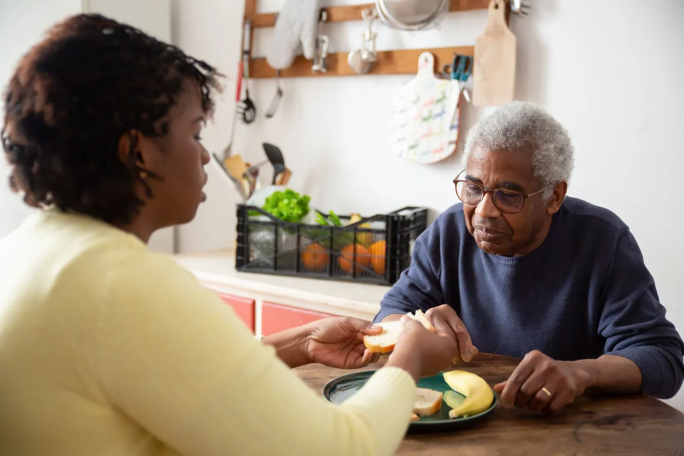 A caregiver helping a man with Parkinson's disease during a meal at home.
