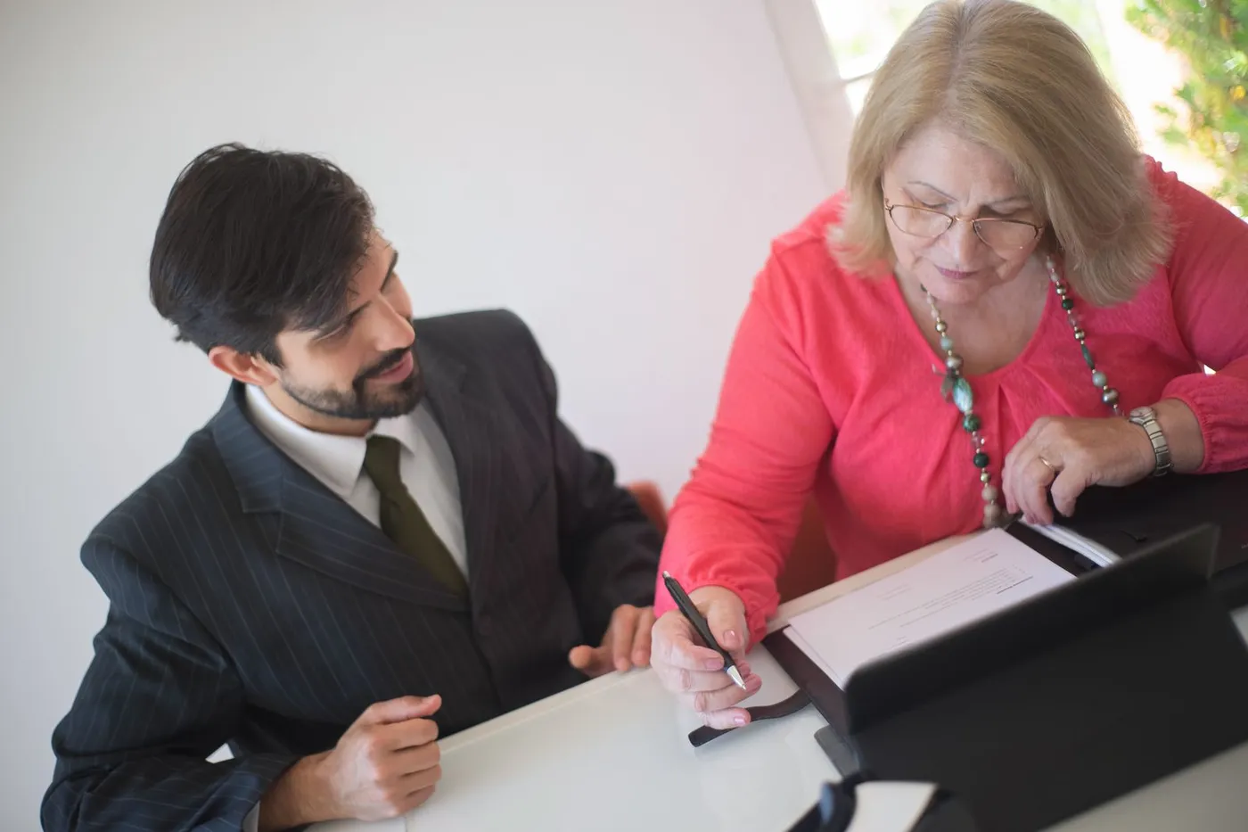 A senior woman signing legal paperwork with a professional assisting her at a desk.