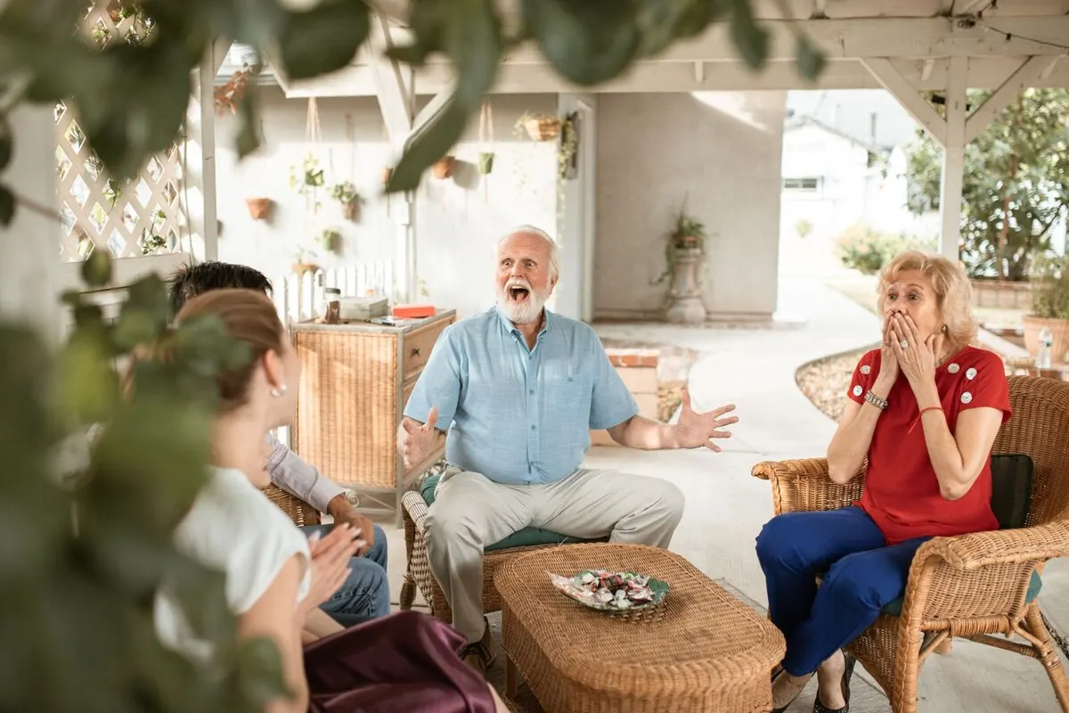 An older couple in conversation with a family member around a table at home.