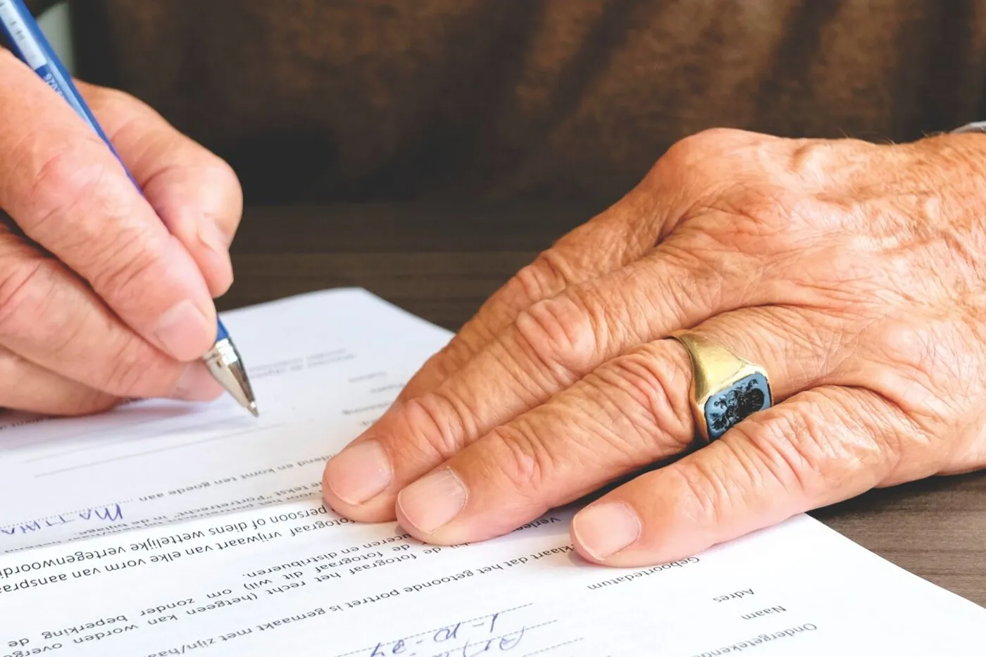 A close-up of an older person's hand signing a printed document with a pen.