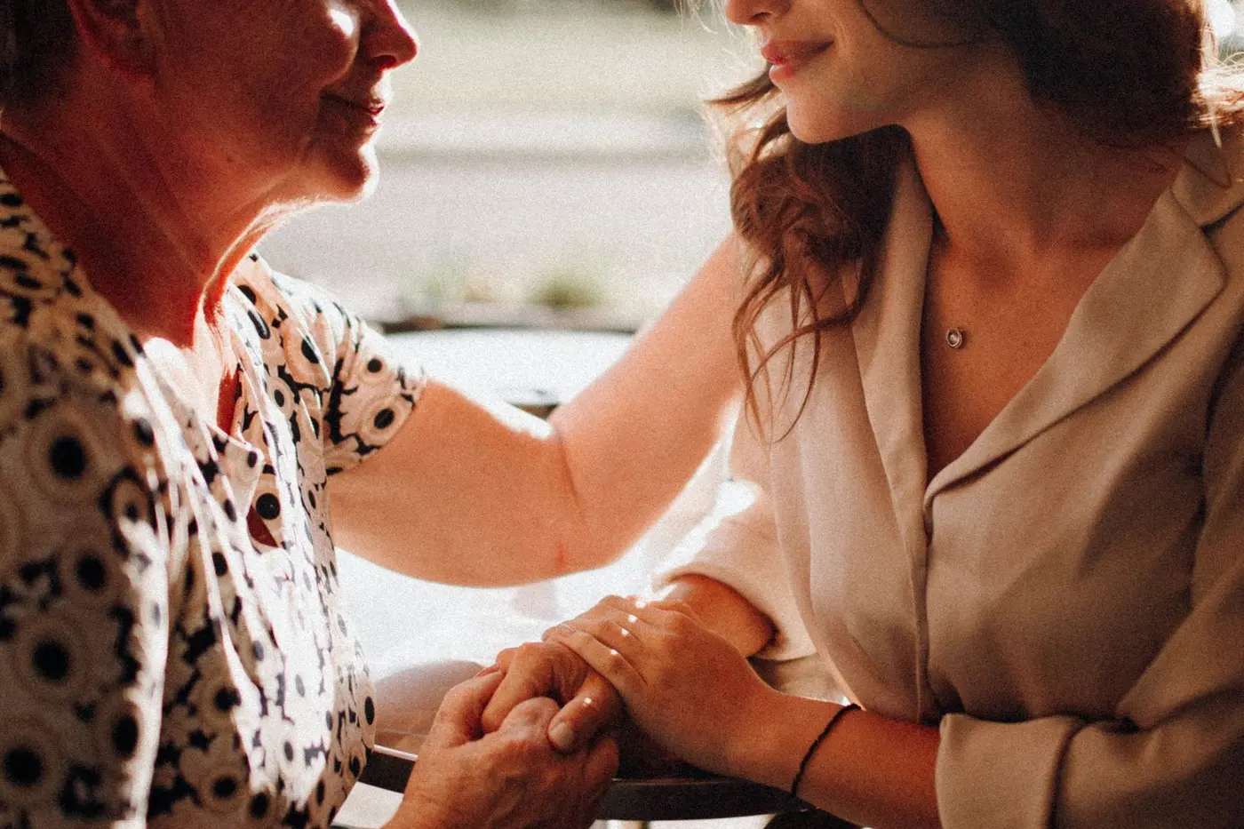 An adult daughter holding her elderly mother's hand across a table.