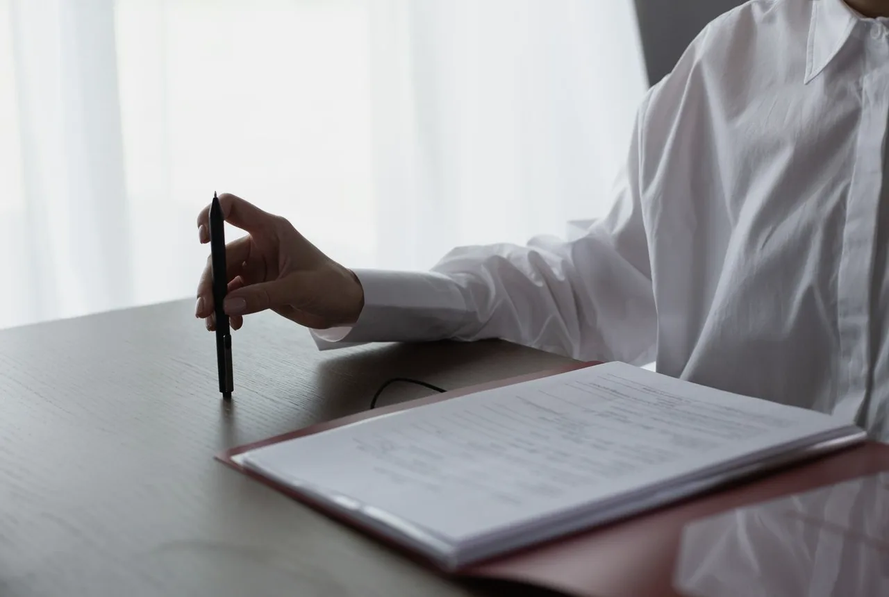 A hand holding a pen, poised over an open contract, pausing before signing.